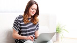 A woman looking at a lap top with a smile as she is making an online booking