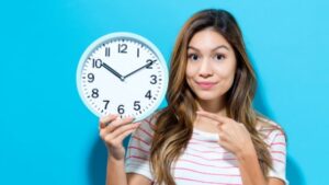 A happy woman holding up a large clock for time-saving salon appointment scheduling